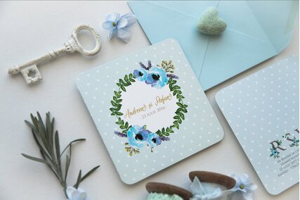 invitatie patrata albastru deschis cu buline albe si coronita de flori albastre cu frunze