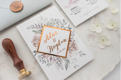 invitatie eleganta cu flori si verdeata cu text rose gold si banda geometrica aurie cu sigiliu